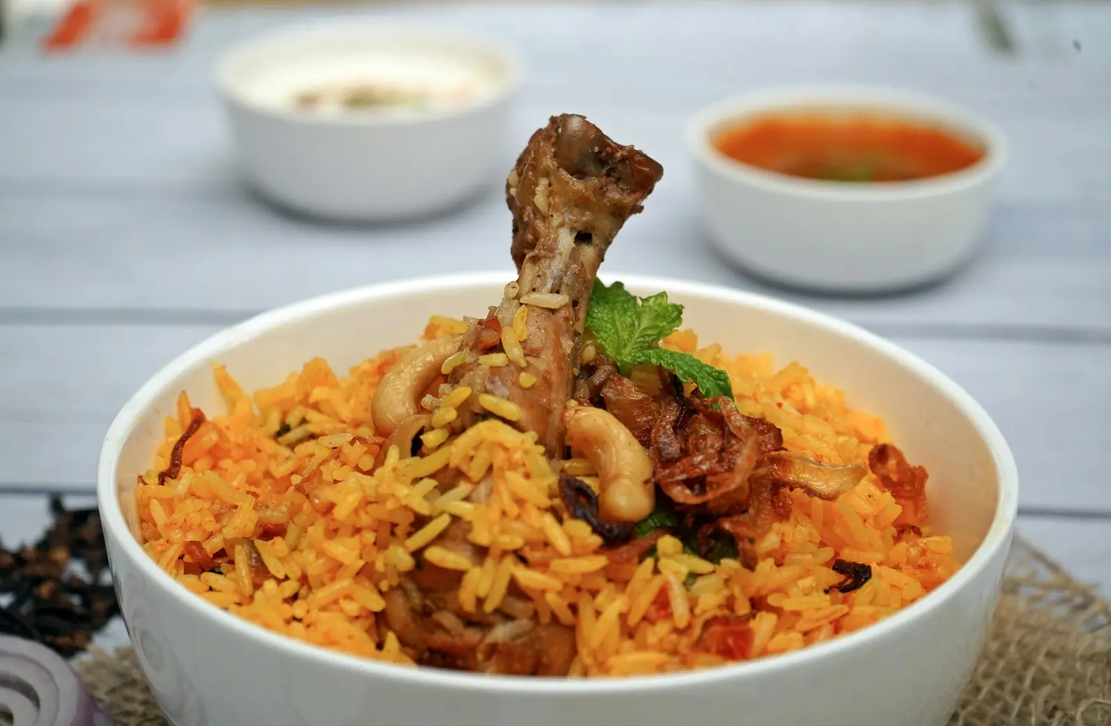 Bowl of chicken biryani with raita and gravy on the side