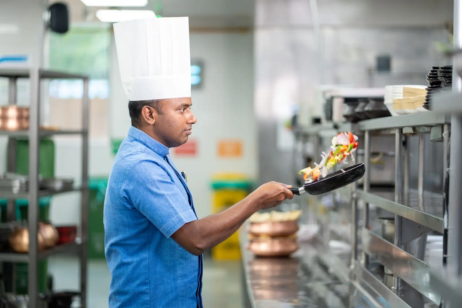 Chef tossing vegetables in a pan in a clean commercial kitchen